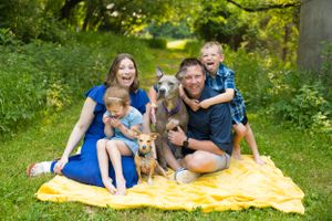 Happy family with children and dogs posing together on a yellow blanket in a lush green park.