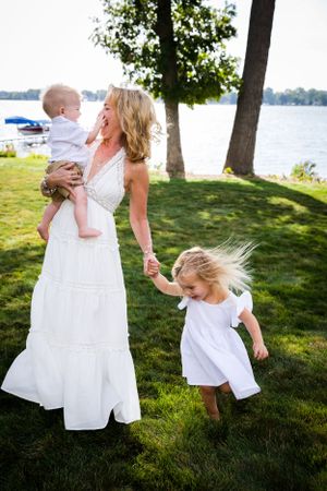 Mother in white dress playing with children by a lakeside on a sunny day.