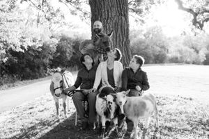 Black and white photo of a group sitting with their dogs under a large tree.