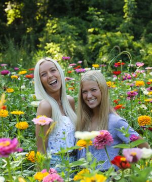 Two people smile while sitting in a vibrant garden of colorful zinnias and wildflowers.