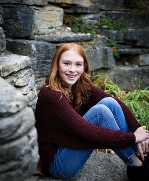 Portrait of a person sitting against stone wall wearing burgundy sweater and jeans.
