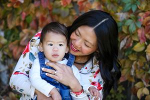 Parent and child share tender moment against backdrop of fall foliage.