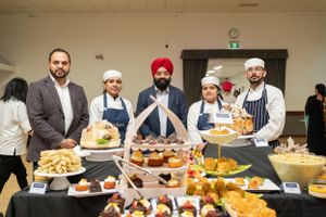 Five men posing behind an elegant dessert and appetizer display table at a catering event.