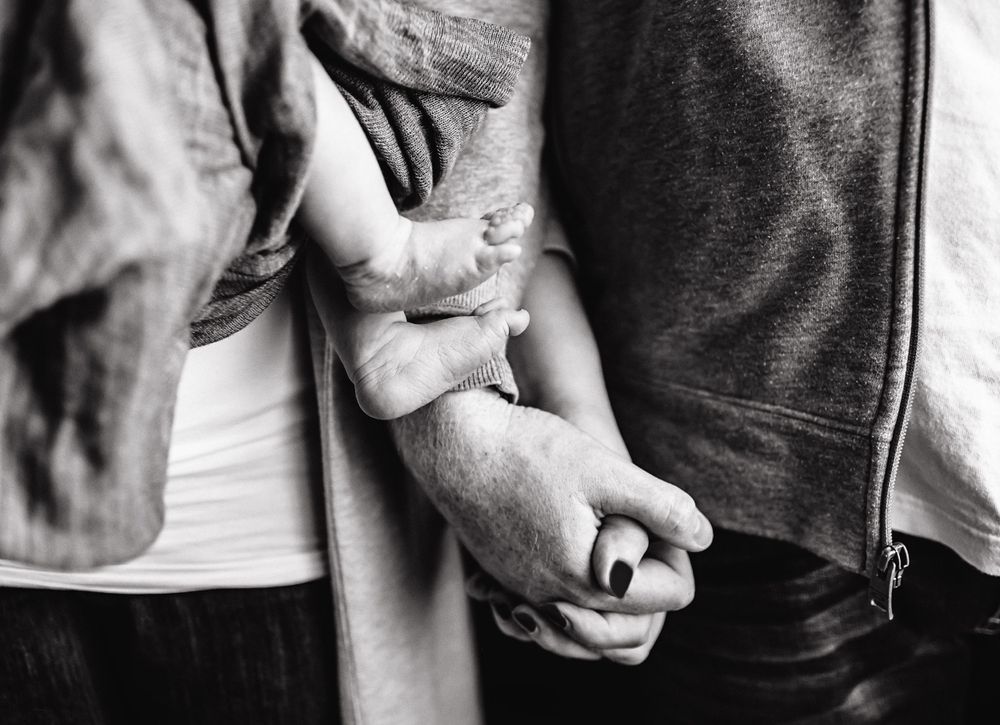 A black and white close-up of hands holding a small baby's hand.