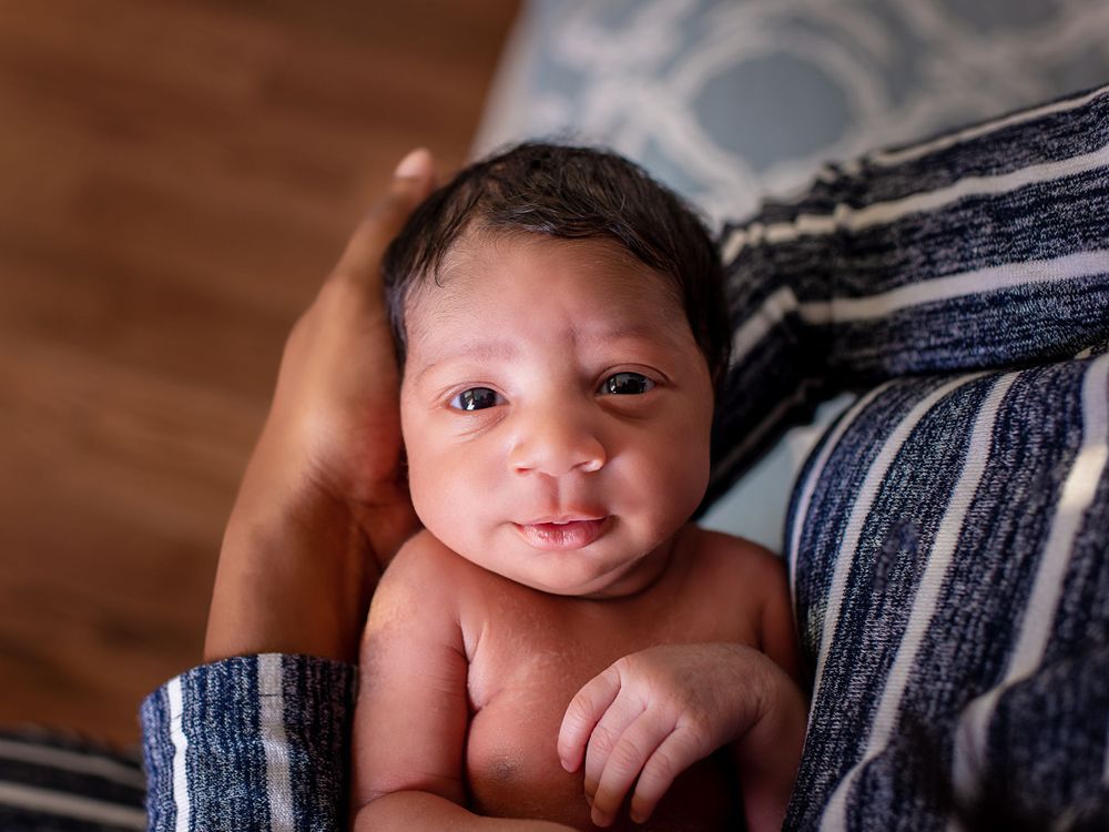 A newborn baby with dark hair wrapped in a blue striped blanket smiles at the camera.