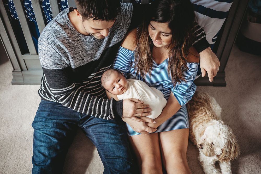 Family relaxing on floor with newborn baby and white dog in nursery.