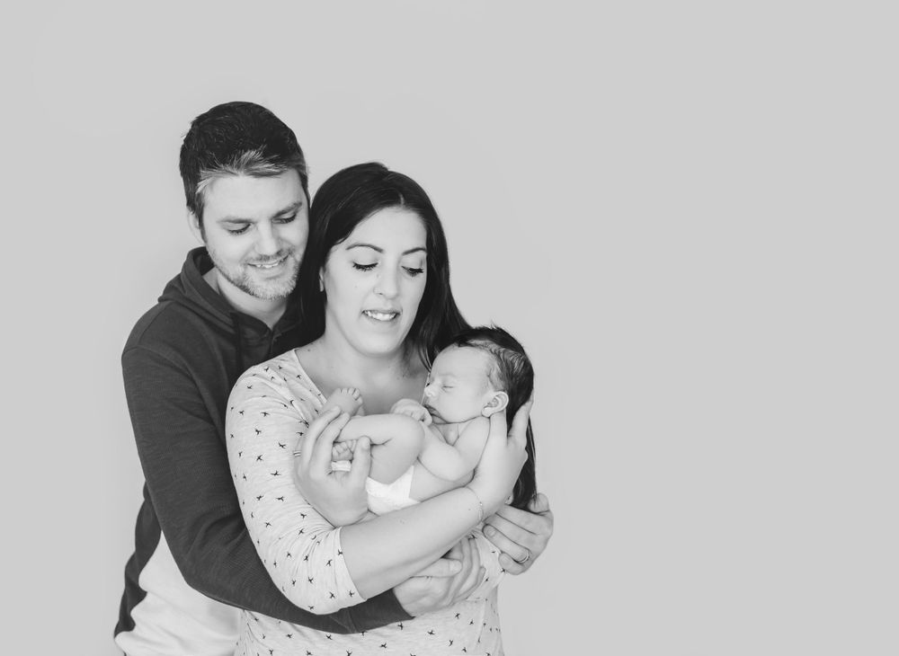 A tender black and white family portrait showing parents embracing their newborn baby.