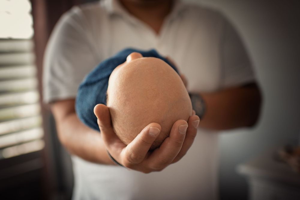 Hands holding a baby doll's head against a soft-focused background.