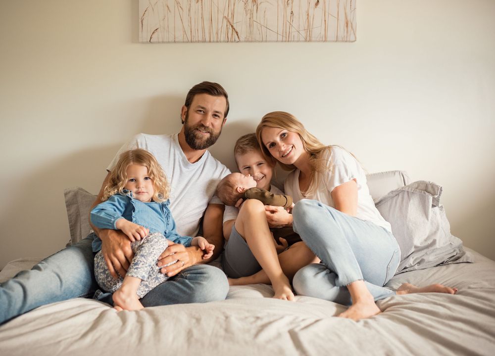 A casual family portrait on a bed with soft natural lighting and neutral decor.