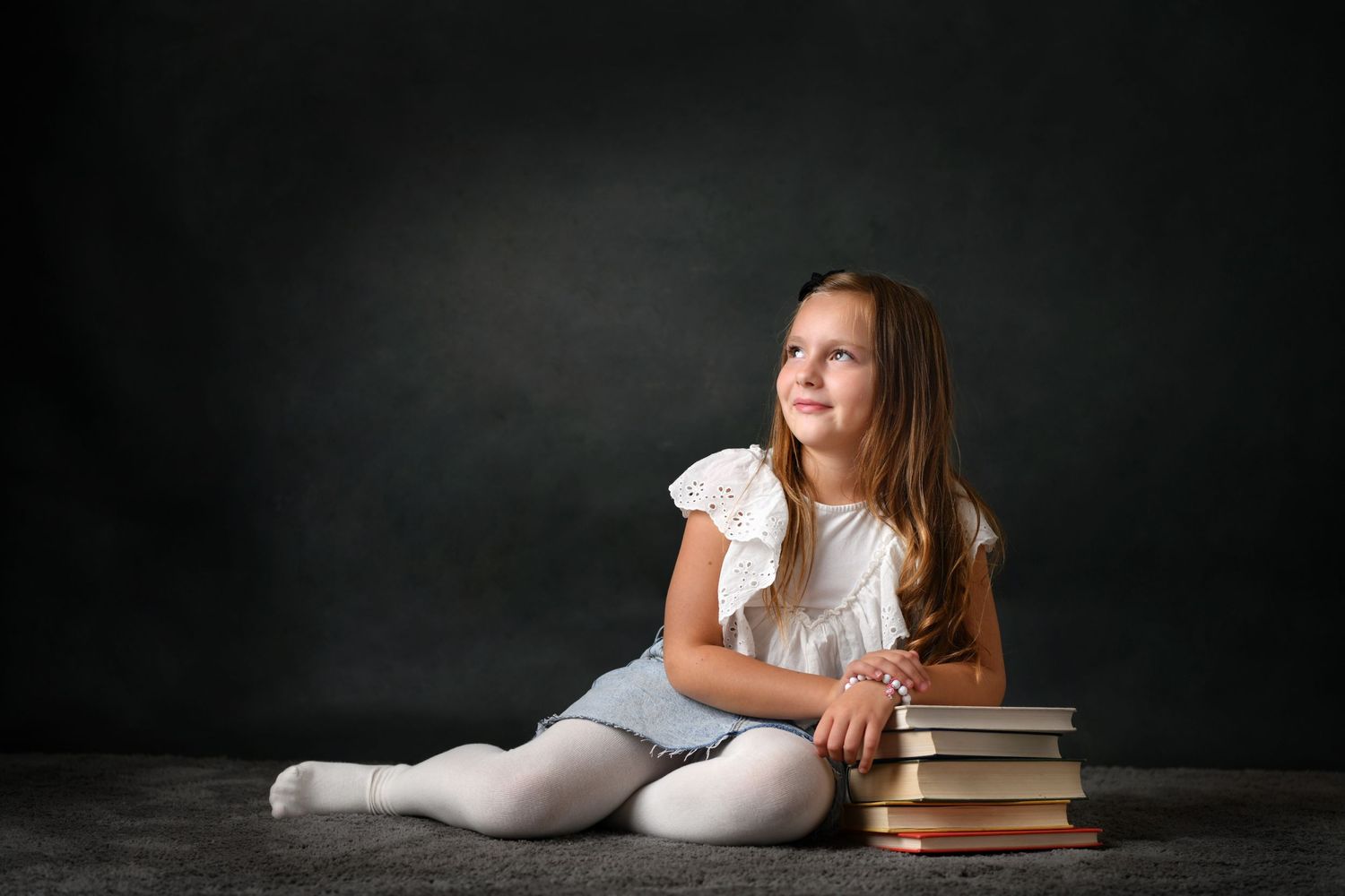 Studio portrait with books and ballet outfit against dark background.