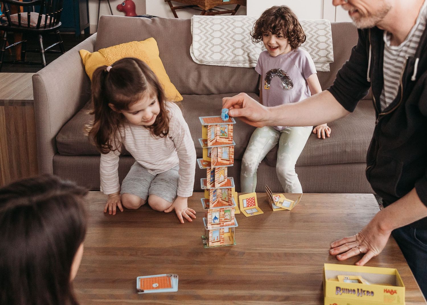 Family gathered around playing with wooden blocks on living room floor.