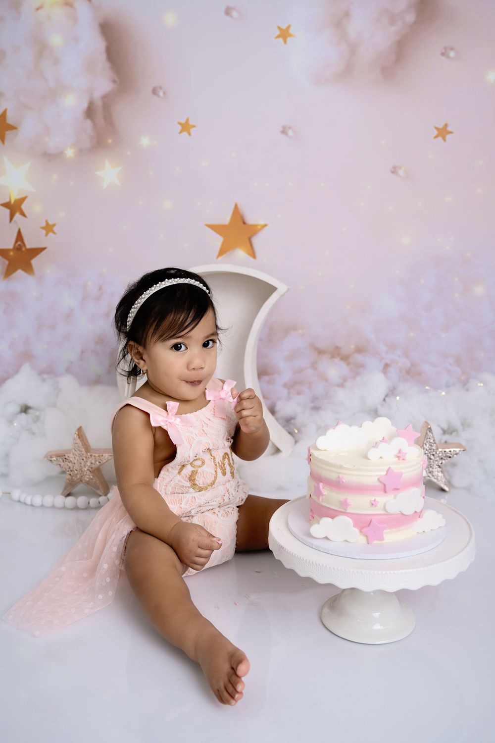 First birthday cake smash session with pink cake on white pedestal against starry backdrop.
