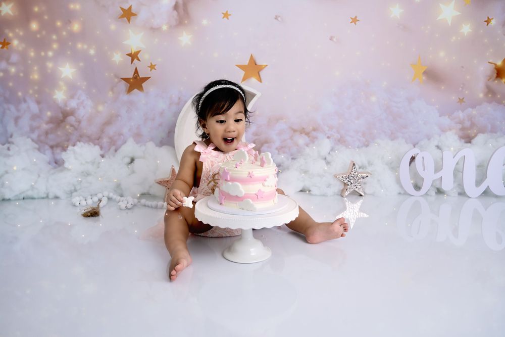 Baby explores pink birthday cake during professional photoshoot with star decorations.