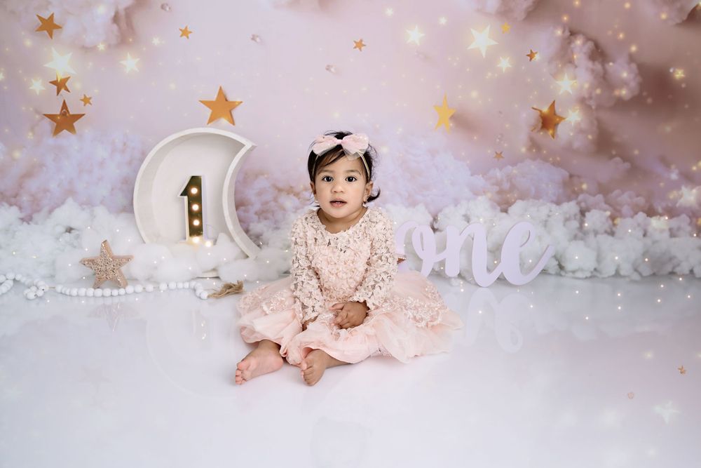 Whimsical cake smash setup with stars and clouds in soft pink and white tones.