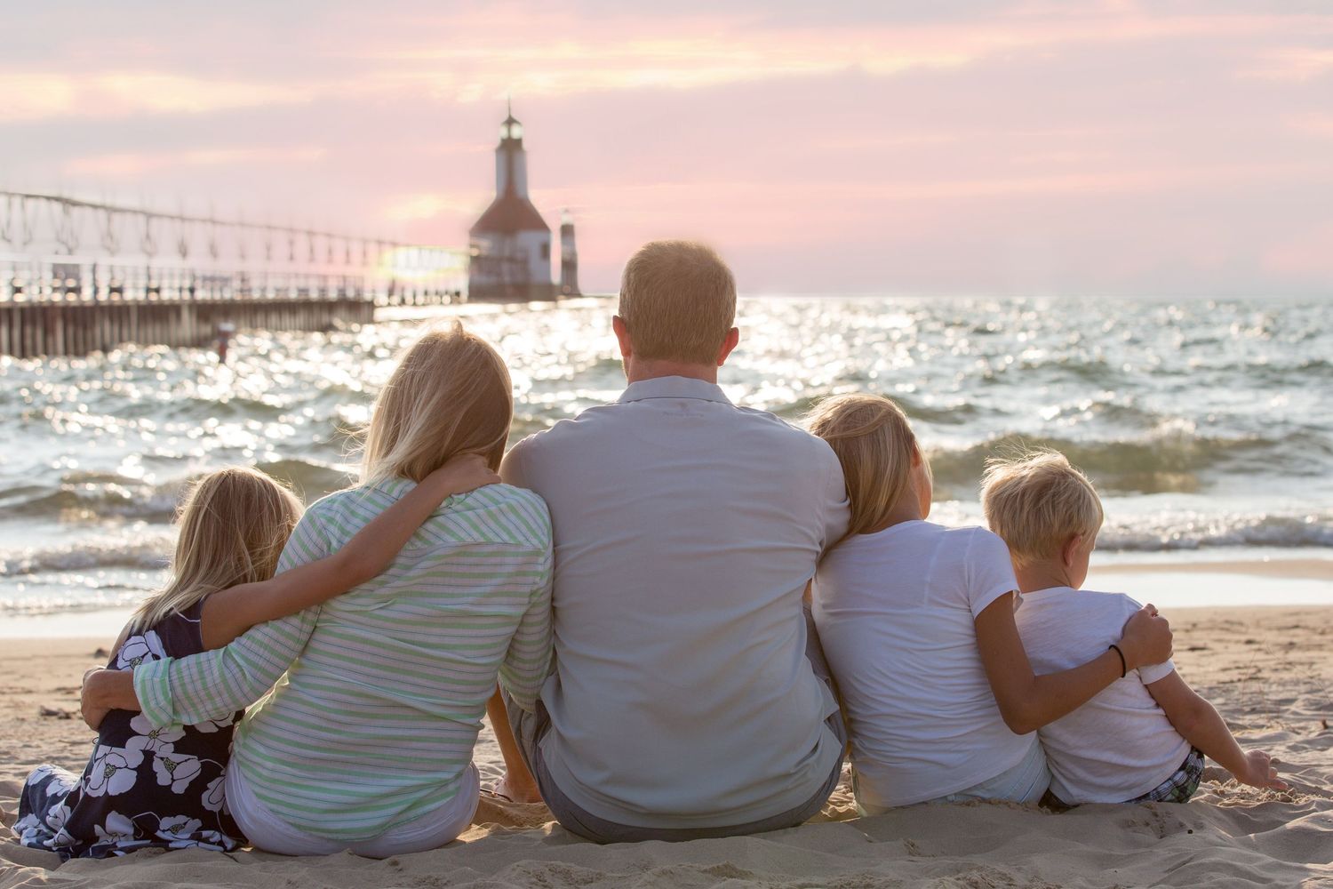 Family sitting together on beach watching sunset near lighthouse.