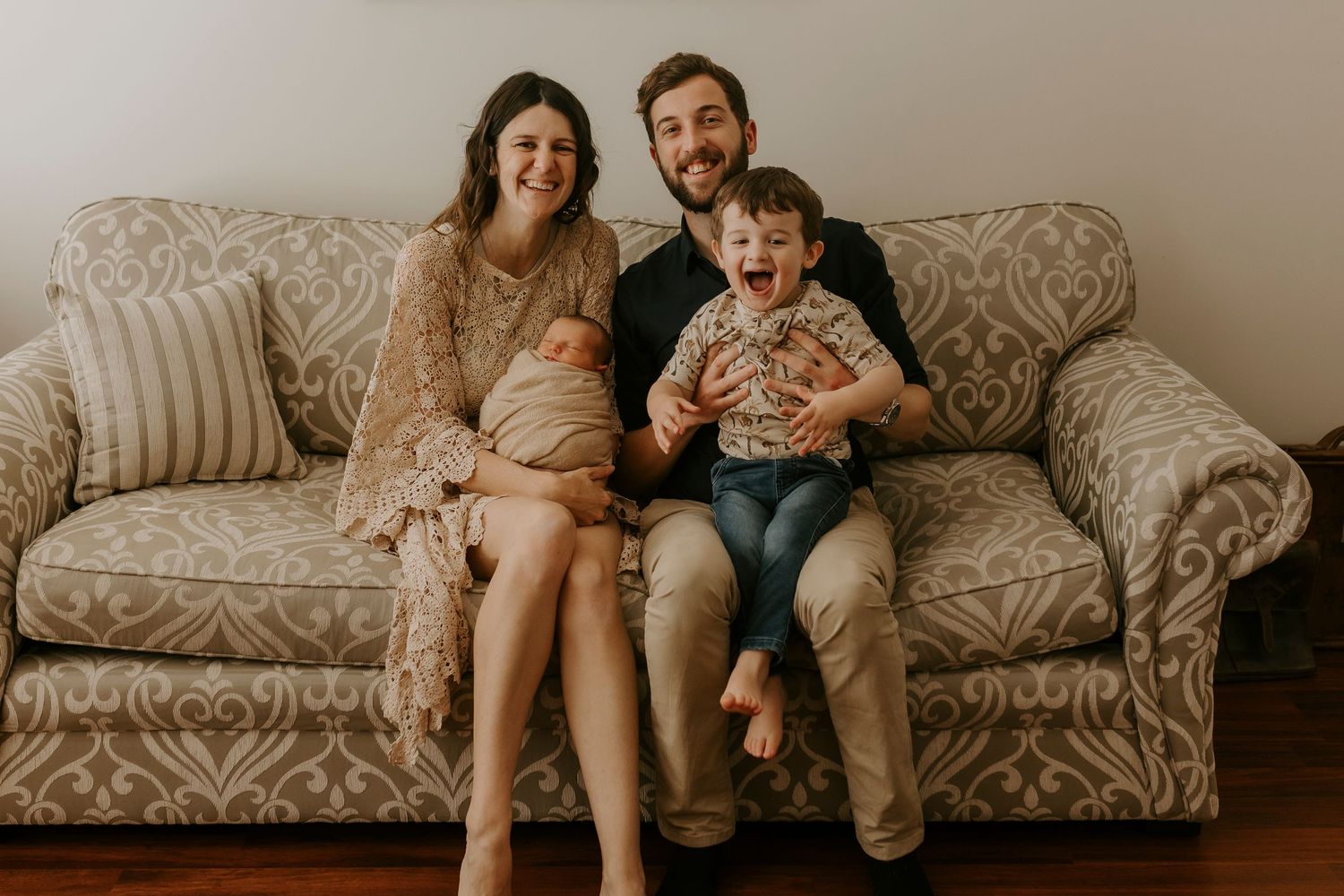 A cozy living room photoshoot showing intimate family moments on a patterned beige couch.