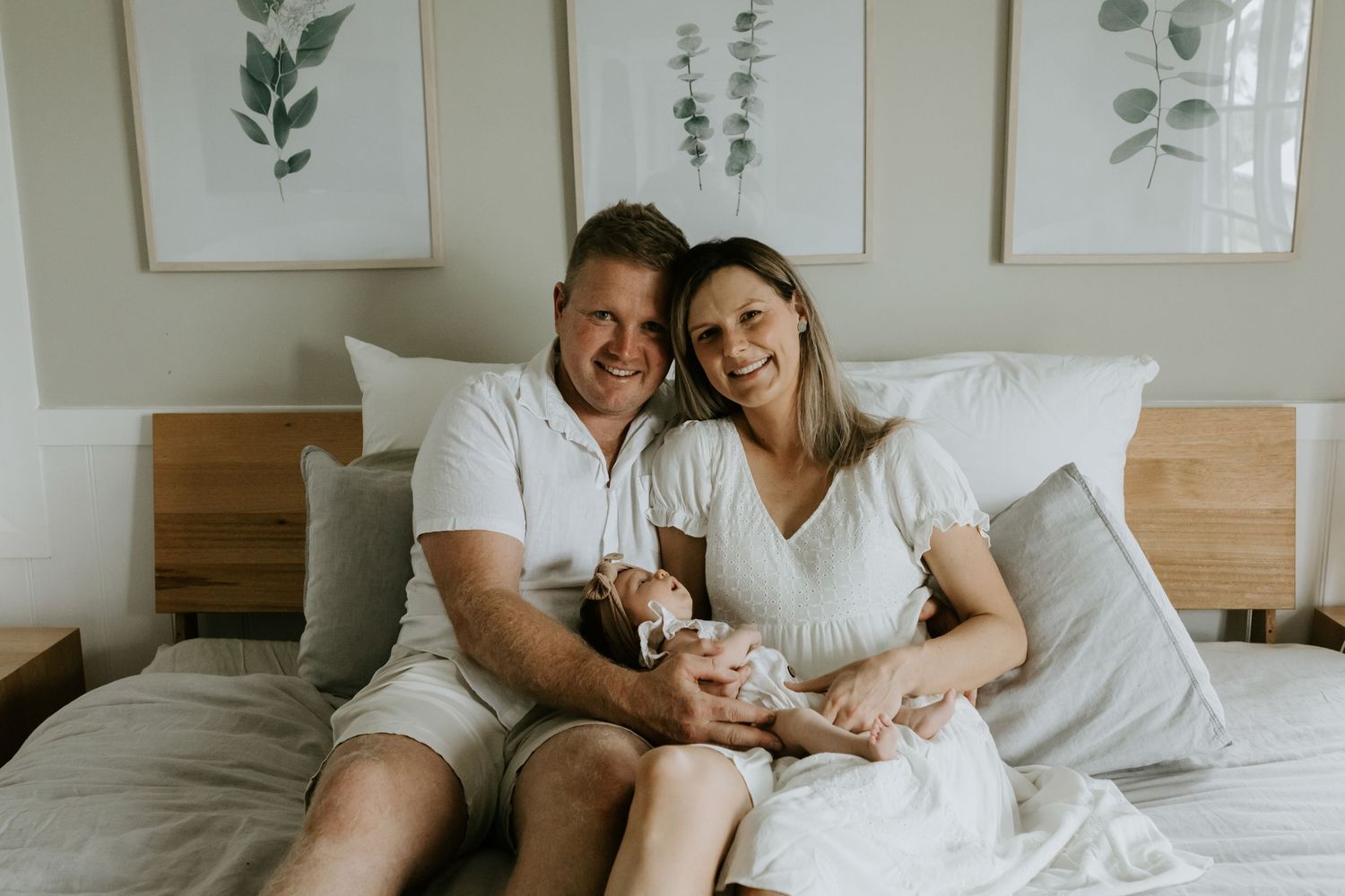 Lifestyle family photography session in a minimalist white bedroom with wooden headboard.