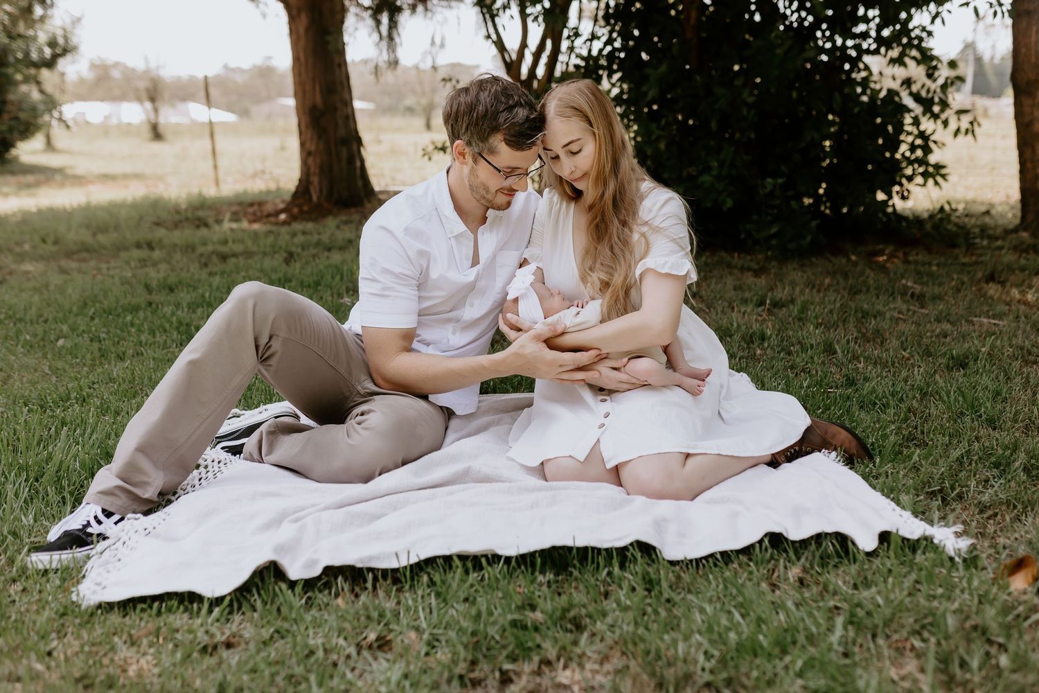 Family relaxes on white blanket during outdoor photography session with their baby.