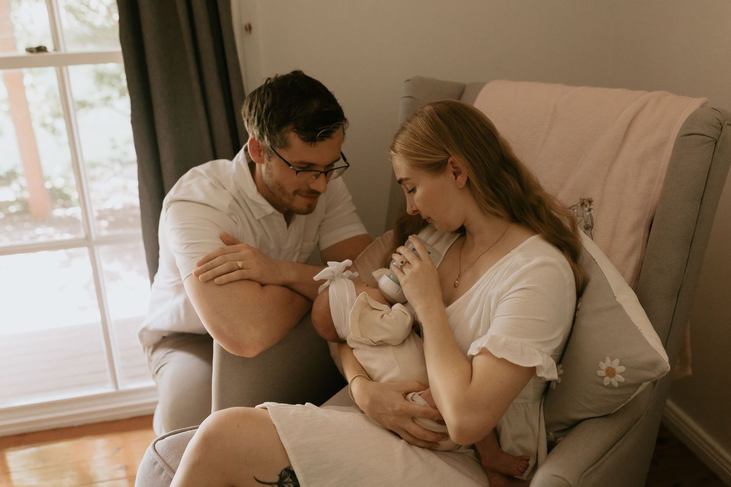 Candid moment captured of couple in white clothing on bed near window.