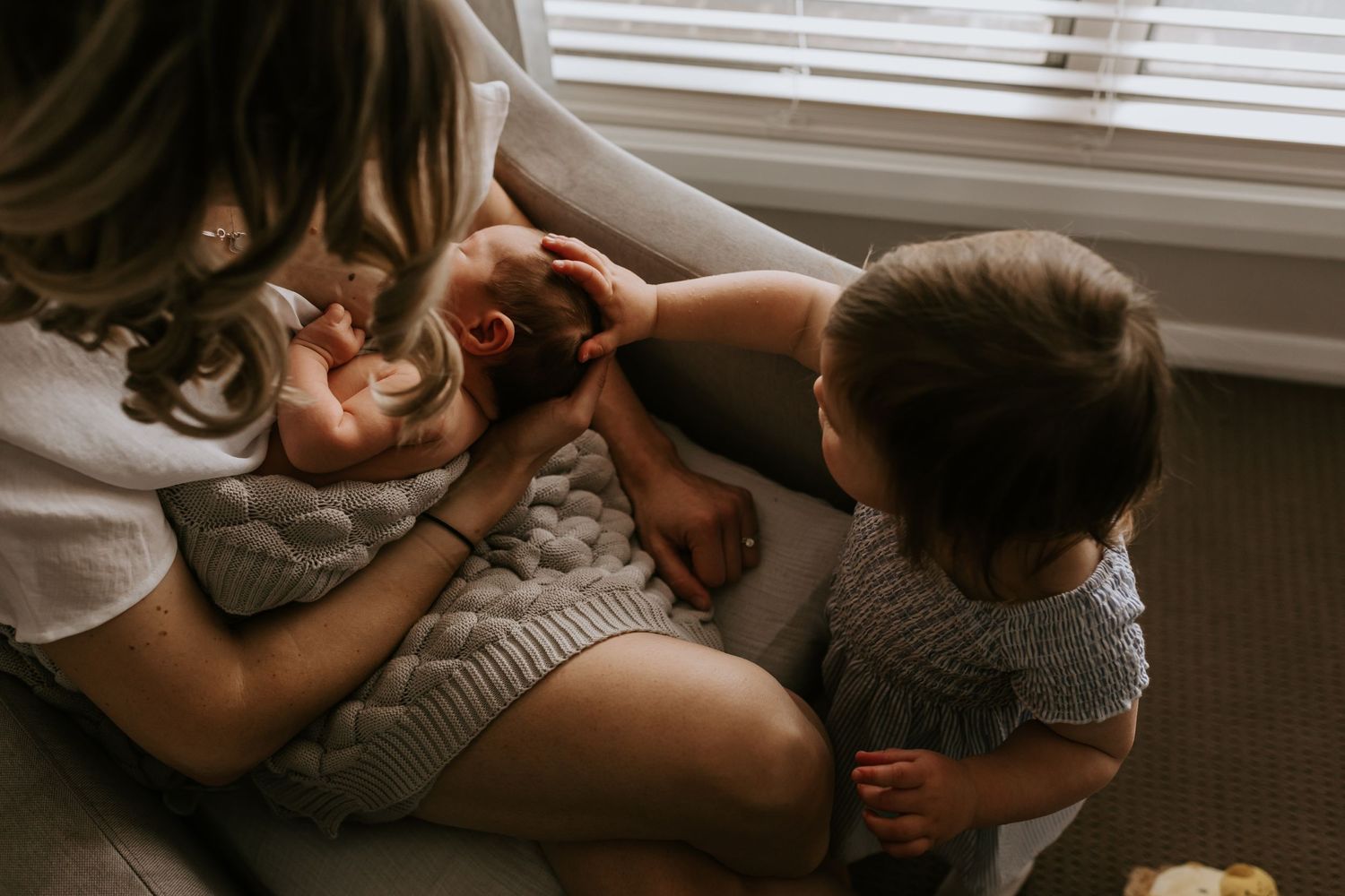 Candid family moments captured in muted tones next to a window with natural light streaming in.