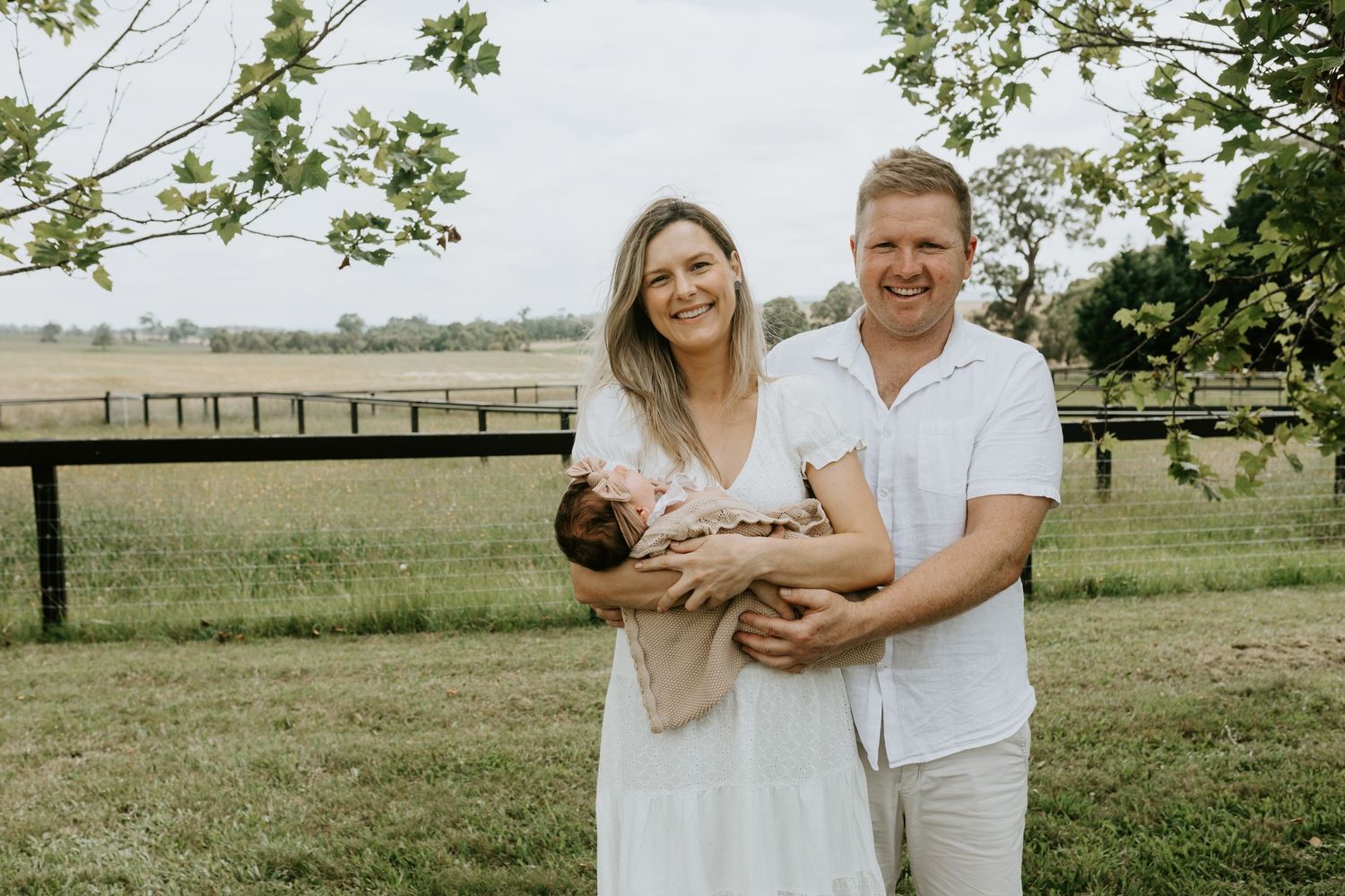 Outdoor family photography session in a rustic field with wooden fence backdrop.