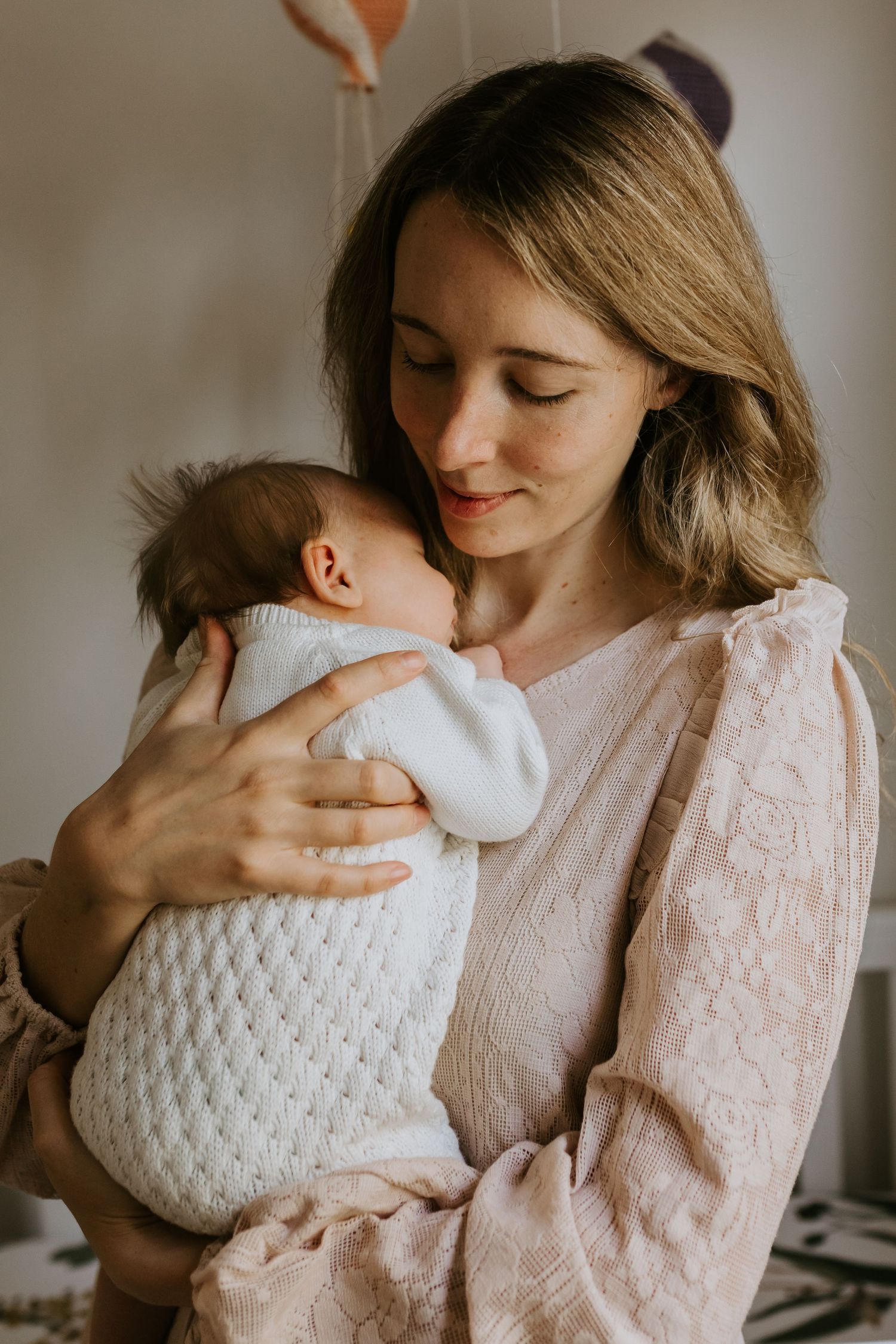 Intimate family photograph showing mother in pink lace holding baby in white knit outfit.