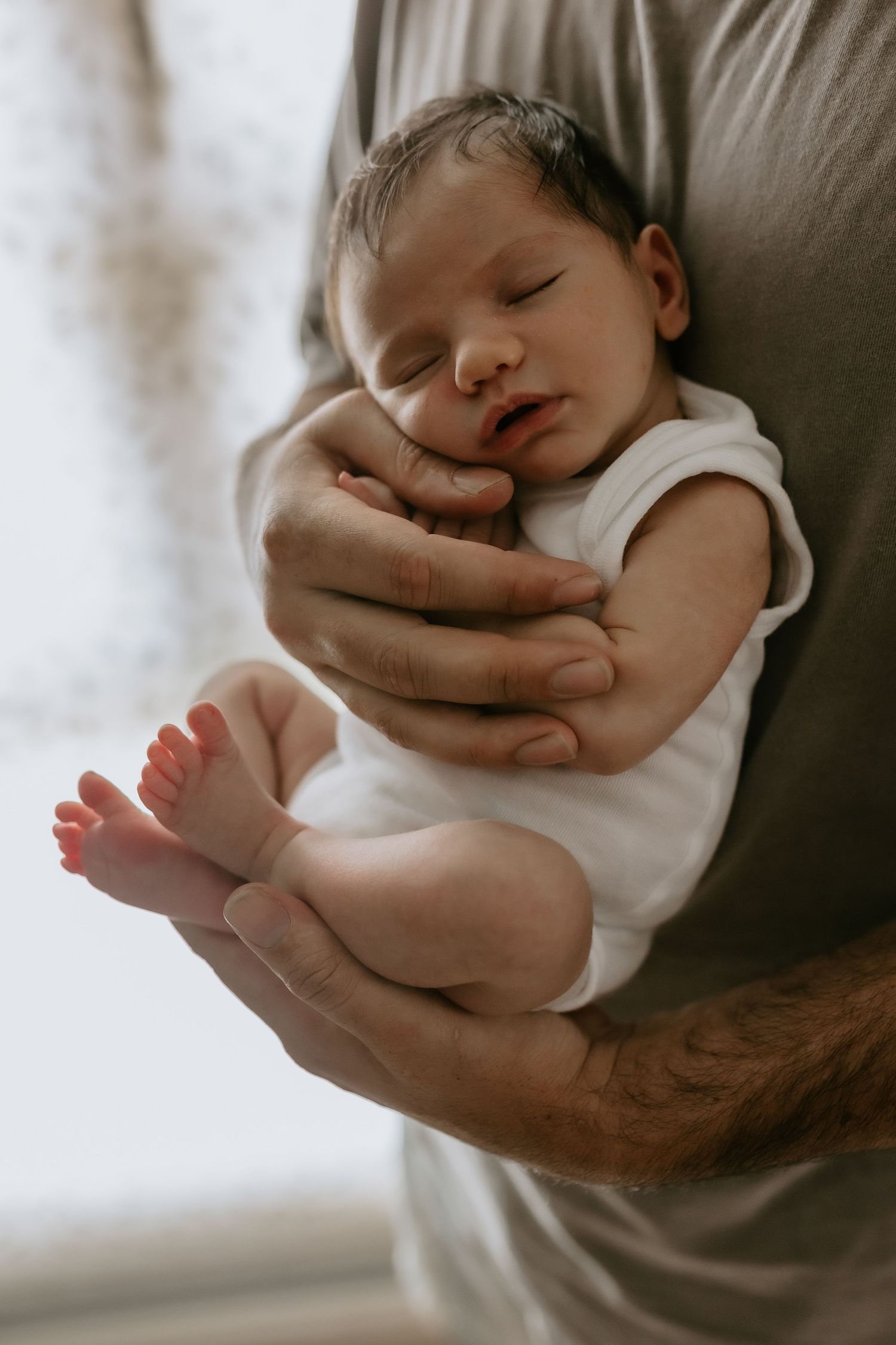 Close-up series showing small sleeping baby cradled in arms wearing white onesie.