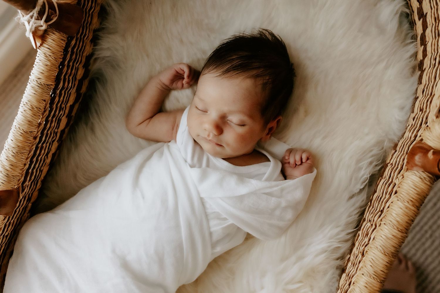 Baby resting on textured beige woven basket during professional newborn photo session.