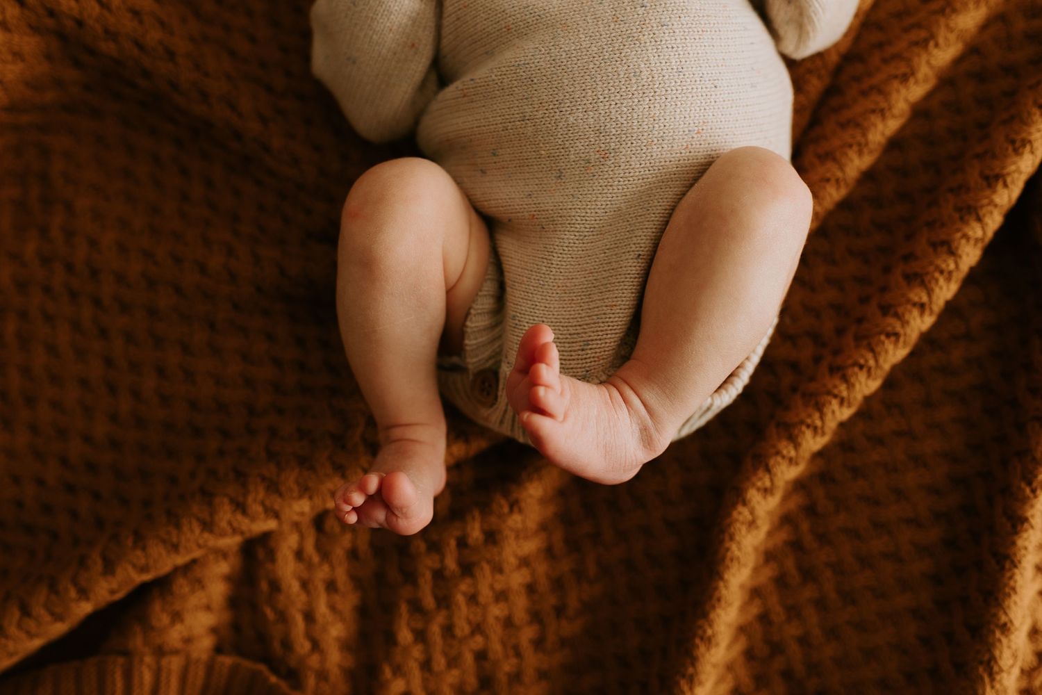 Close-up details of bare feet and knitted orange blanket texture during indoor photoshoot.