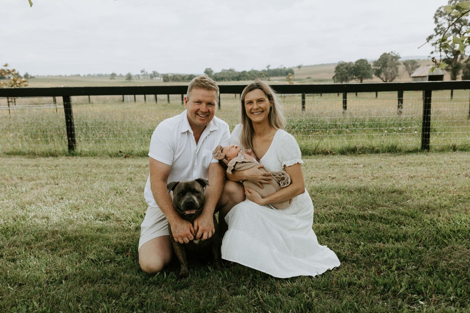 Rural countryside photoshoot with wooden fencing and green pasture in background.
