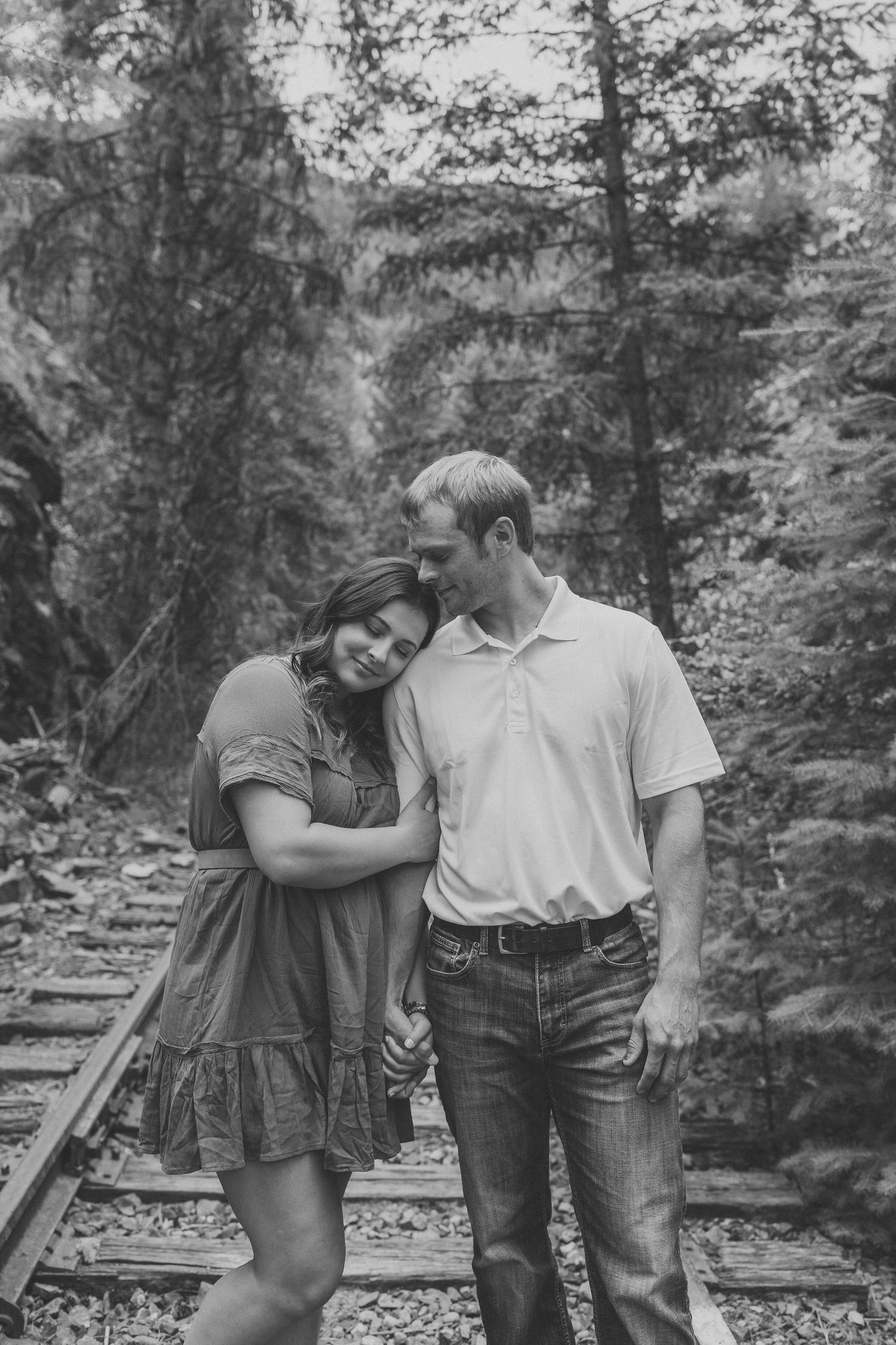 A couple embracing on rustic train tracks surrounded by lush forest.