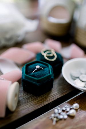 Wedding rings nestled in dark teal velvet ring box with jewelry details.