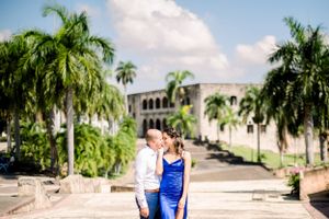 Couple posing on palm tree lined path with beautiful architecture in background.