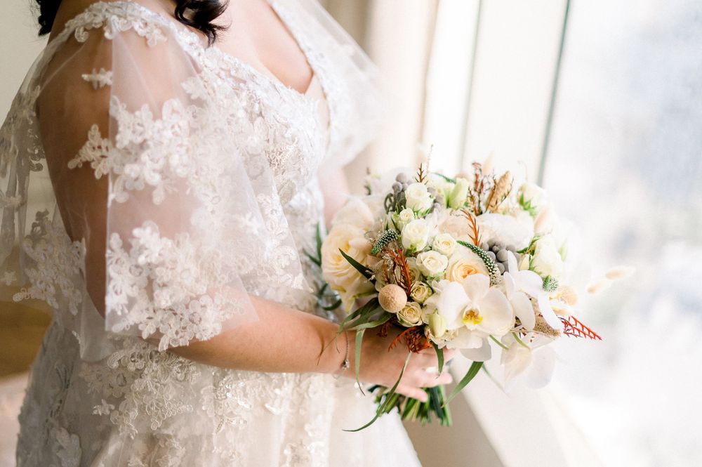 Detail shot of bridal bouquet with peach roses and lace sleeve of wedding dress.