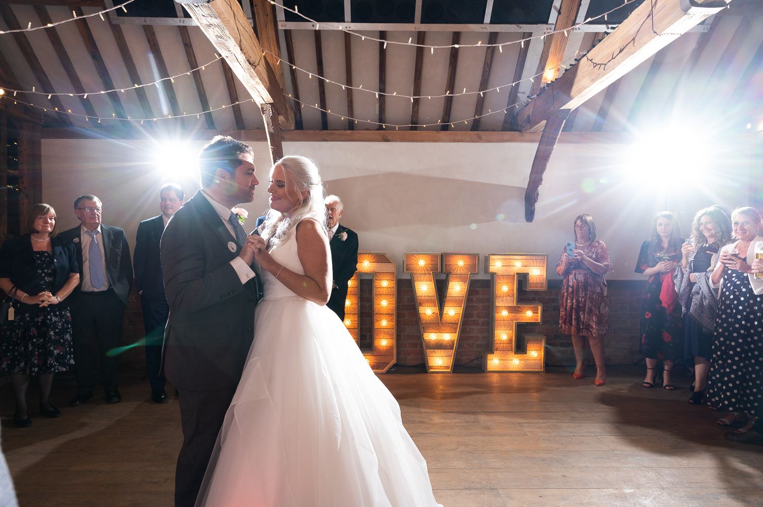 Couple dancing at wedding reception with illuminated LOVE sign in background.