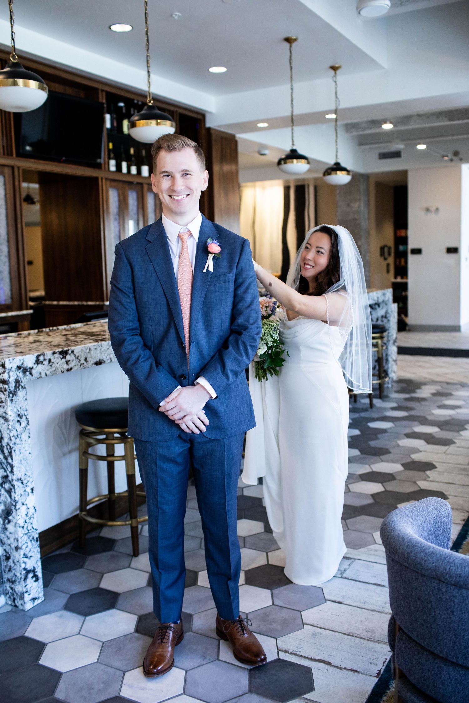 A playful wedding moment in a modern venue with a navy suit and white dress against a geometric tiled floor.
