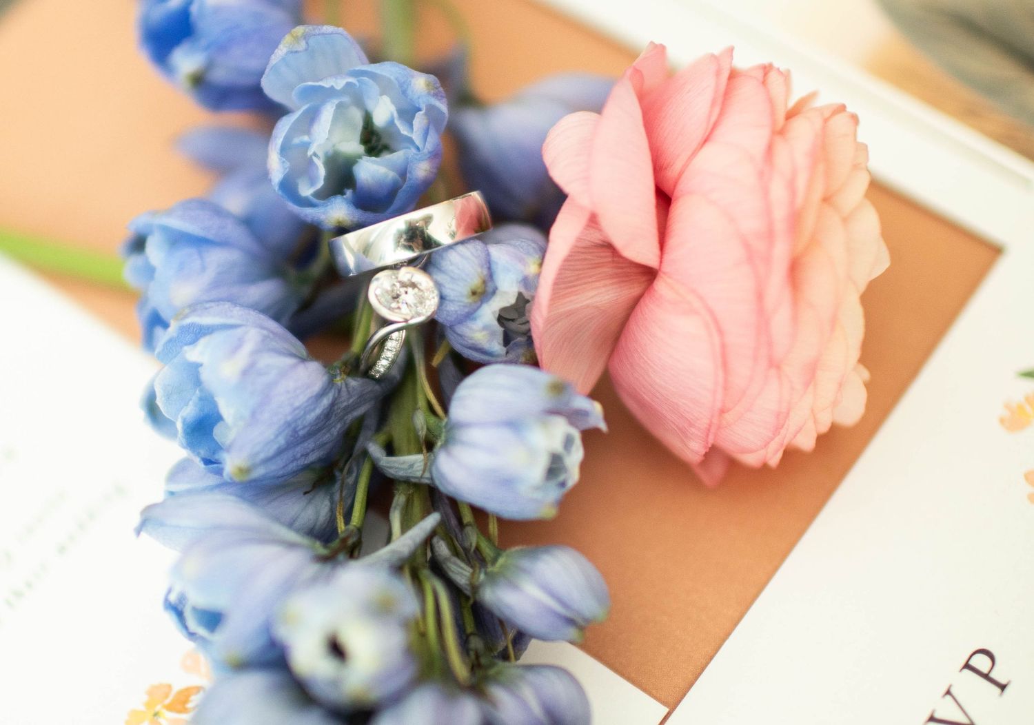 Wedding rings nestled among pink and blue flowers in a delicate arrangement.