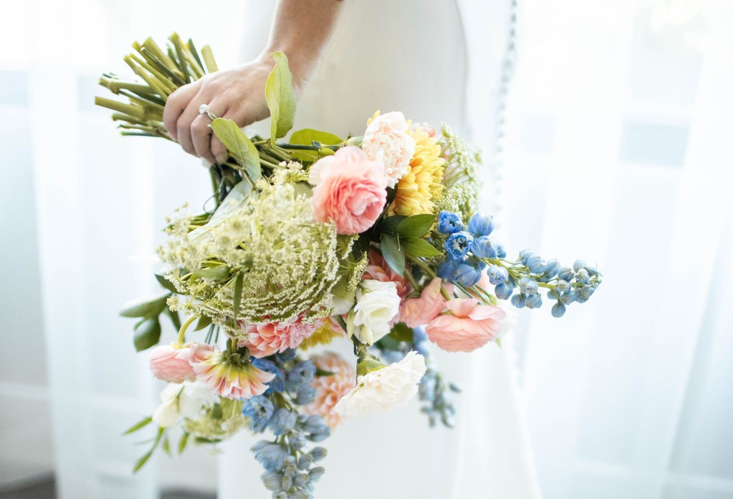 Close-up of bridal bouquet with pink roses, blue delphiniums, and green hydrangeas.