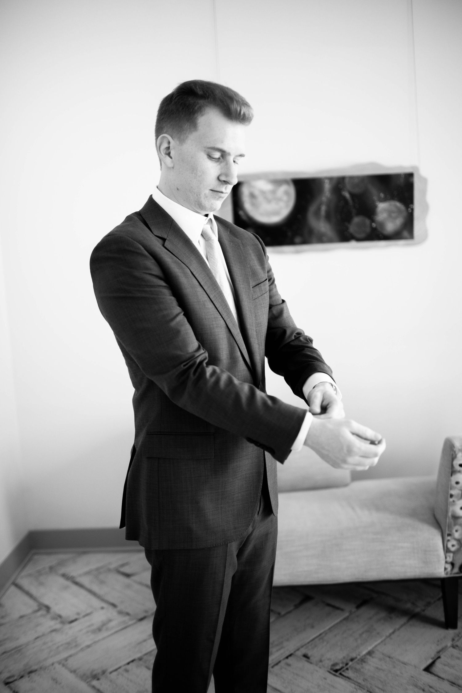 Black and white photo of groom adjusting cufflinks while wearing classic dark suit.