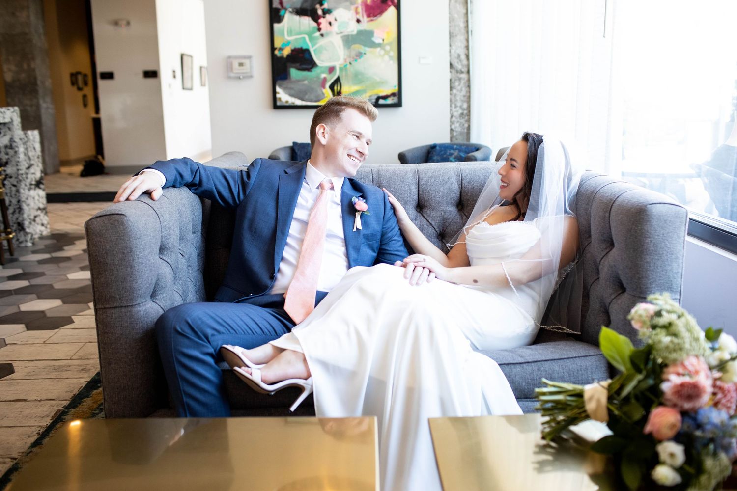 Wedding couple relaxing on a grey couch in a modern lounge setting.