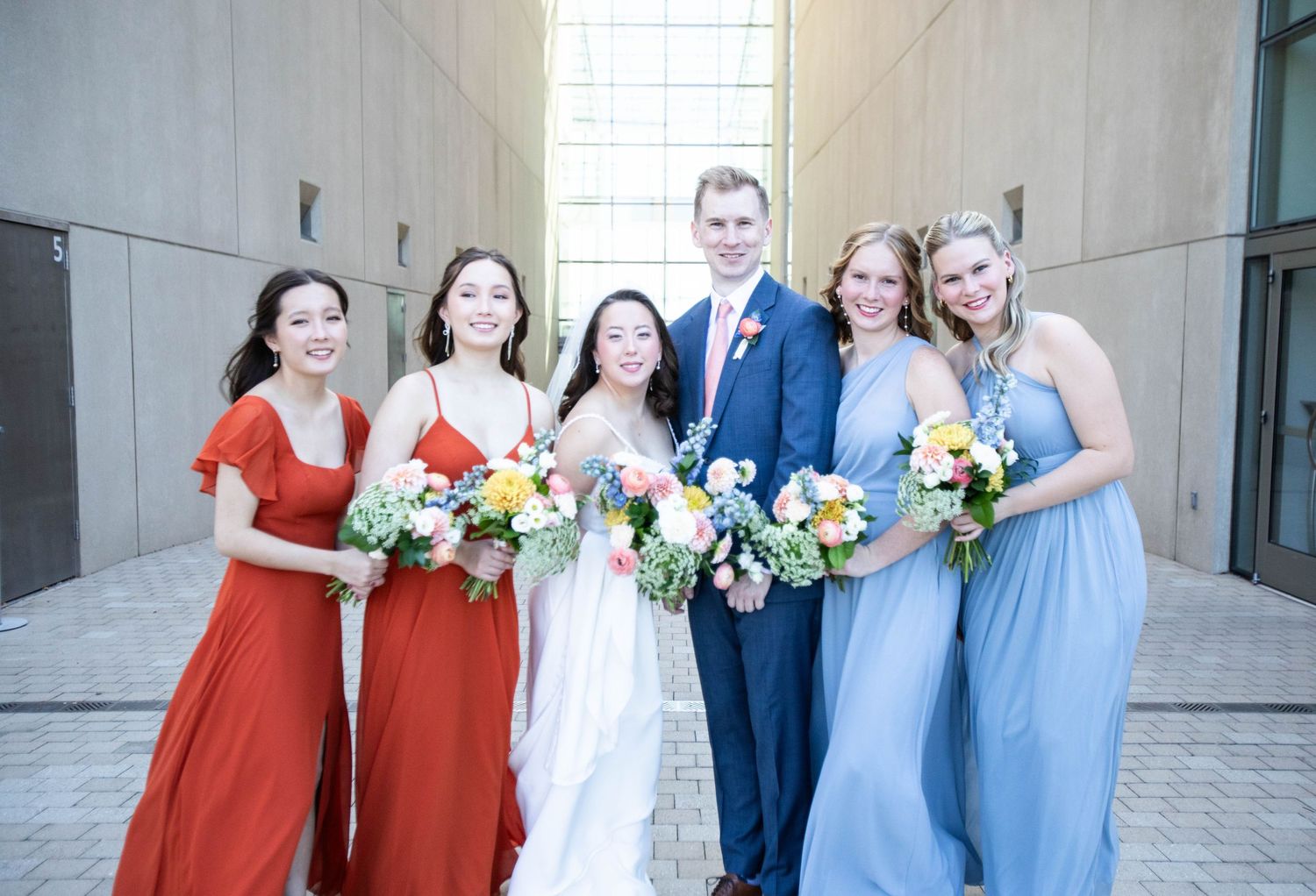 Bridal party in alternating red and blue dresses posing outdoors with bouquets.