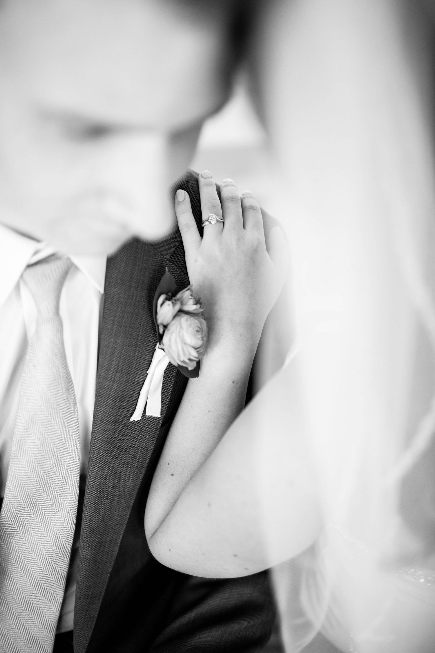 Black and white close-up of boutonniere and hand on groom's lapel.