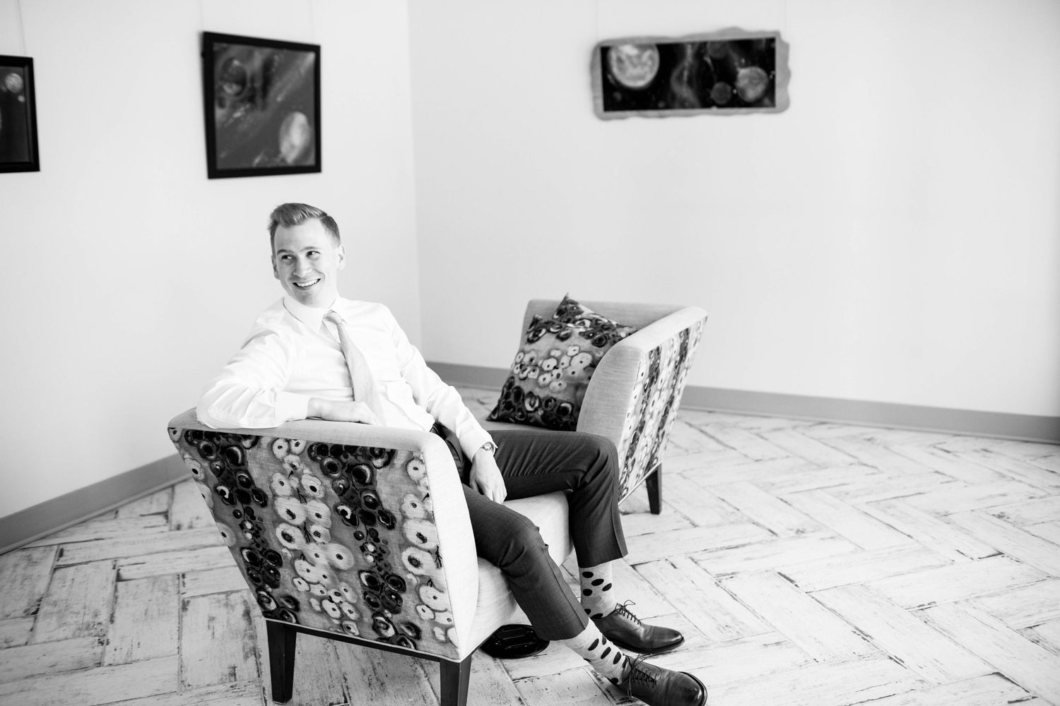 Black and white portrait of person sitting casually in patterned armchair.