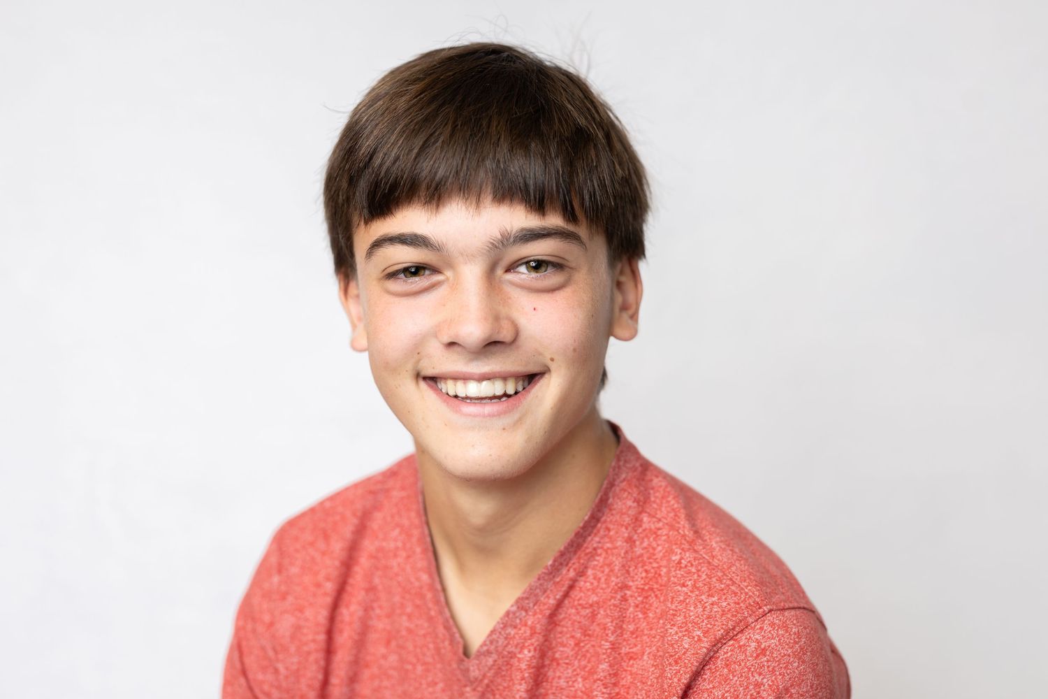 Portrait of a smiling youth in a coral-colored shirt against white background.
