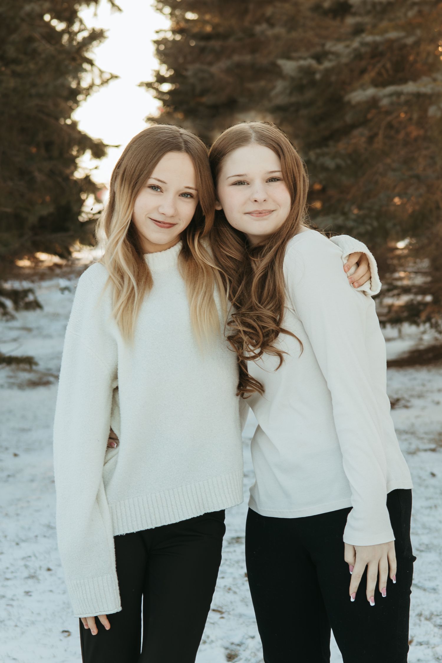 Two friends in matching white sweaters and dark pants pose together in a snowy winter setting.