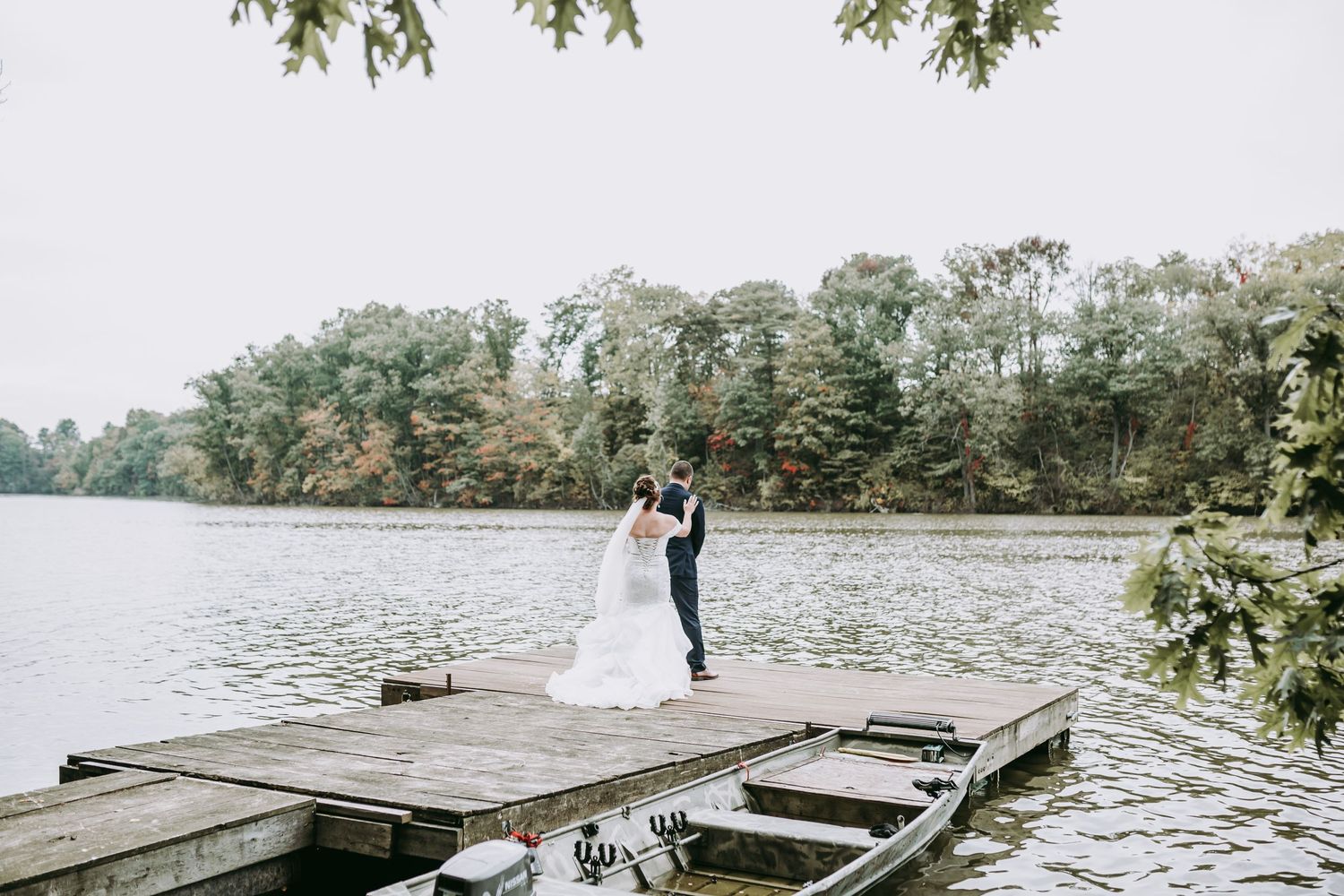 Newlyweds pose together on wooden dock overlooking peaceful lake.