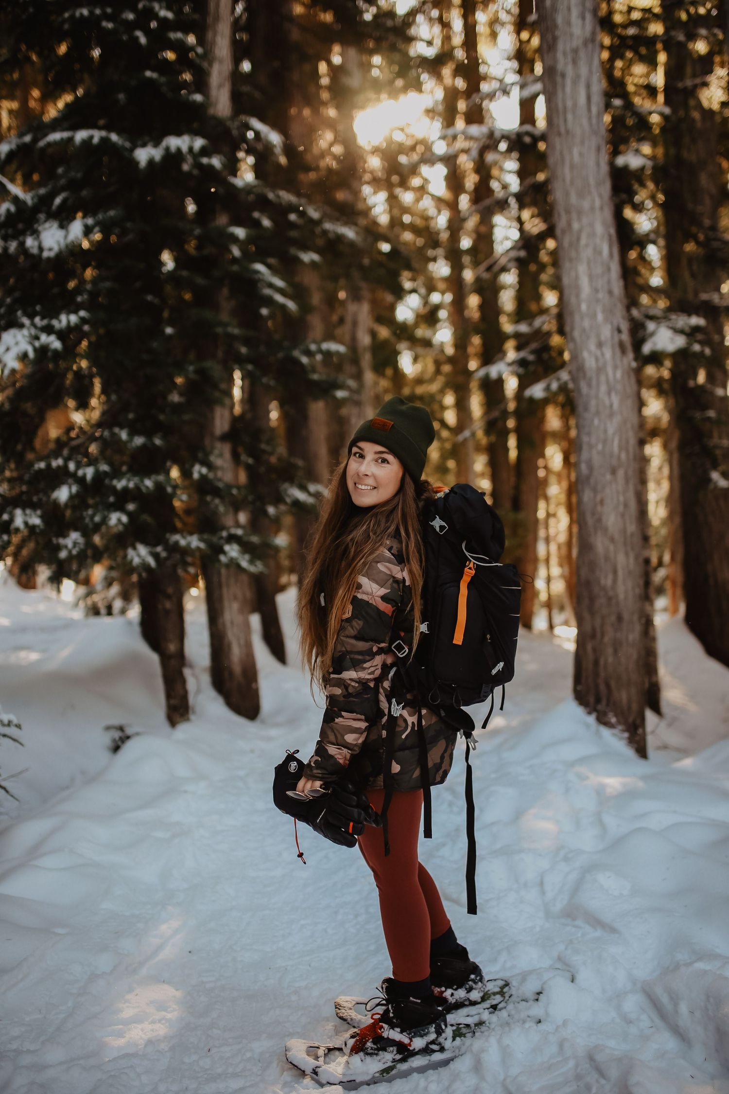 A winter adventurer on snowshoes poses cheerfully in a snowy forest at sunset.