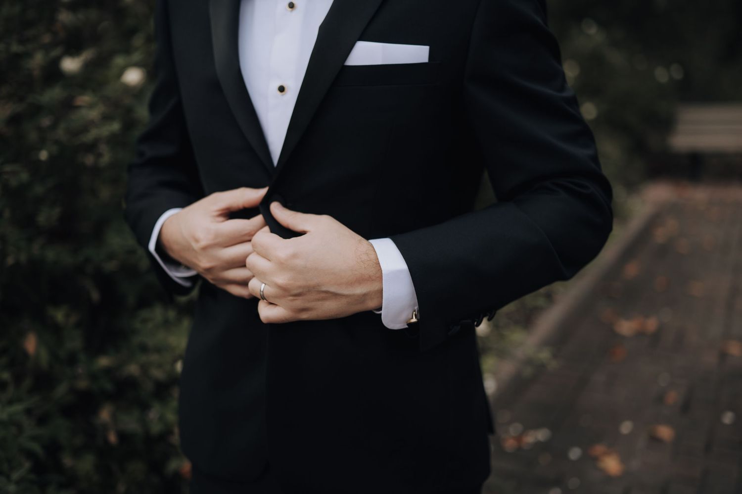 Detail shot of groom adjusting his classic black tuxedo cuff and buttons.