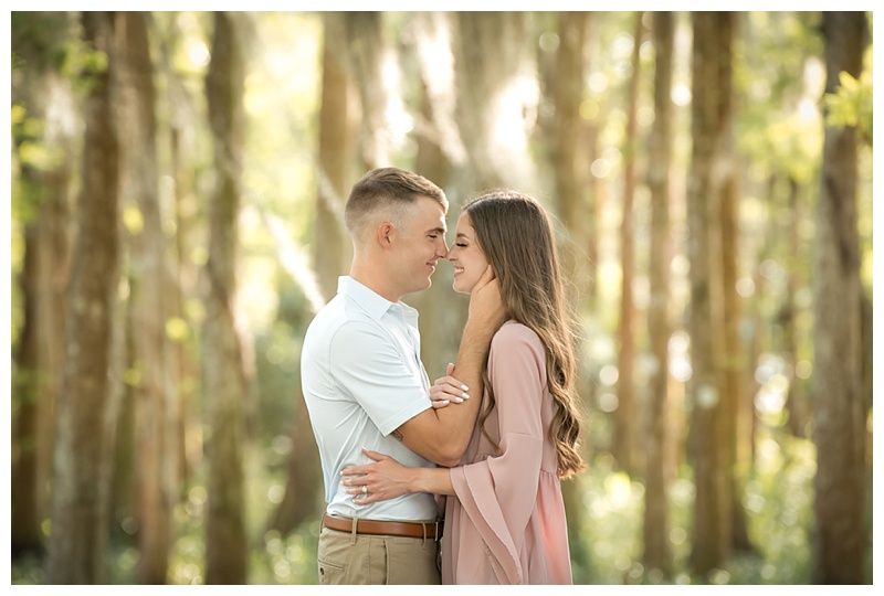 Romantic forest engagement session with golden sunlight filtering through trees.