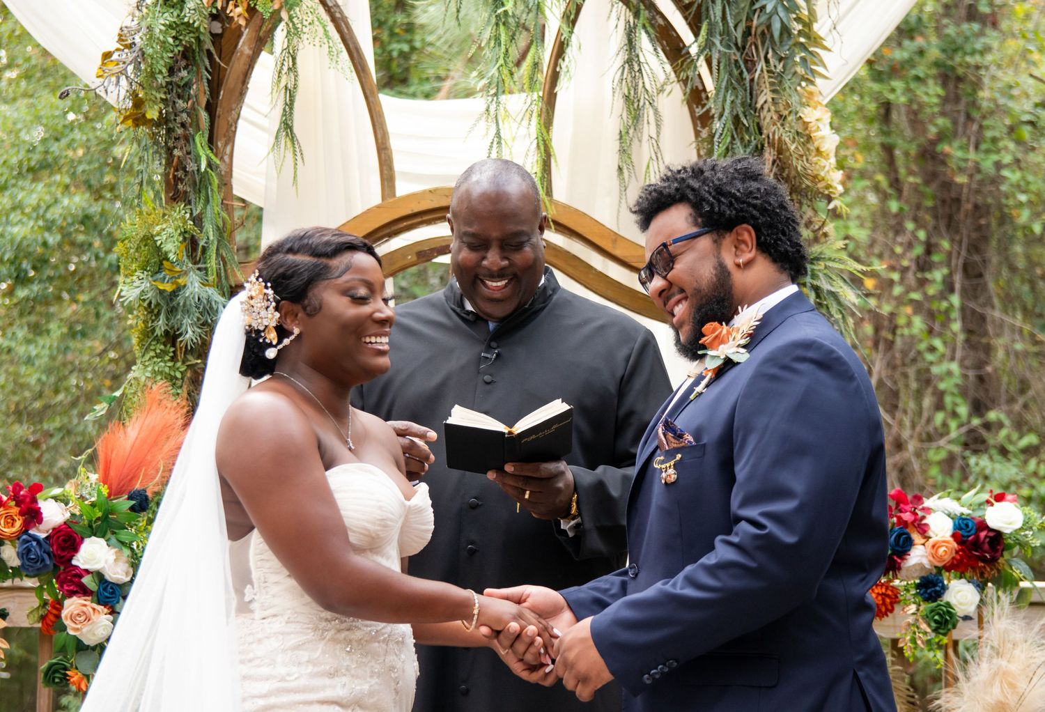 An intimate outdoor wedding ceremony under a floral arch in a lush garden setting.